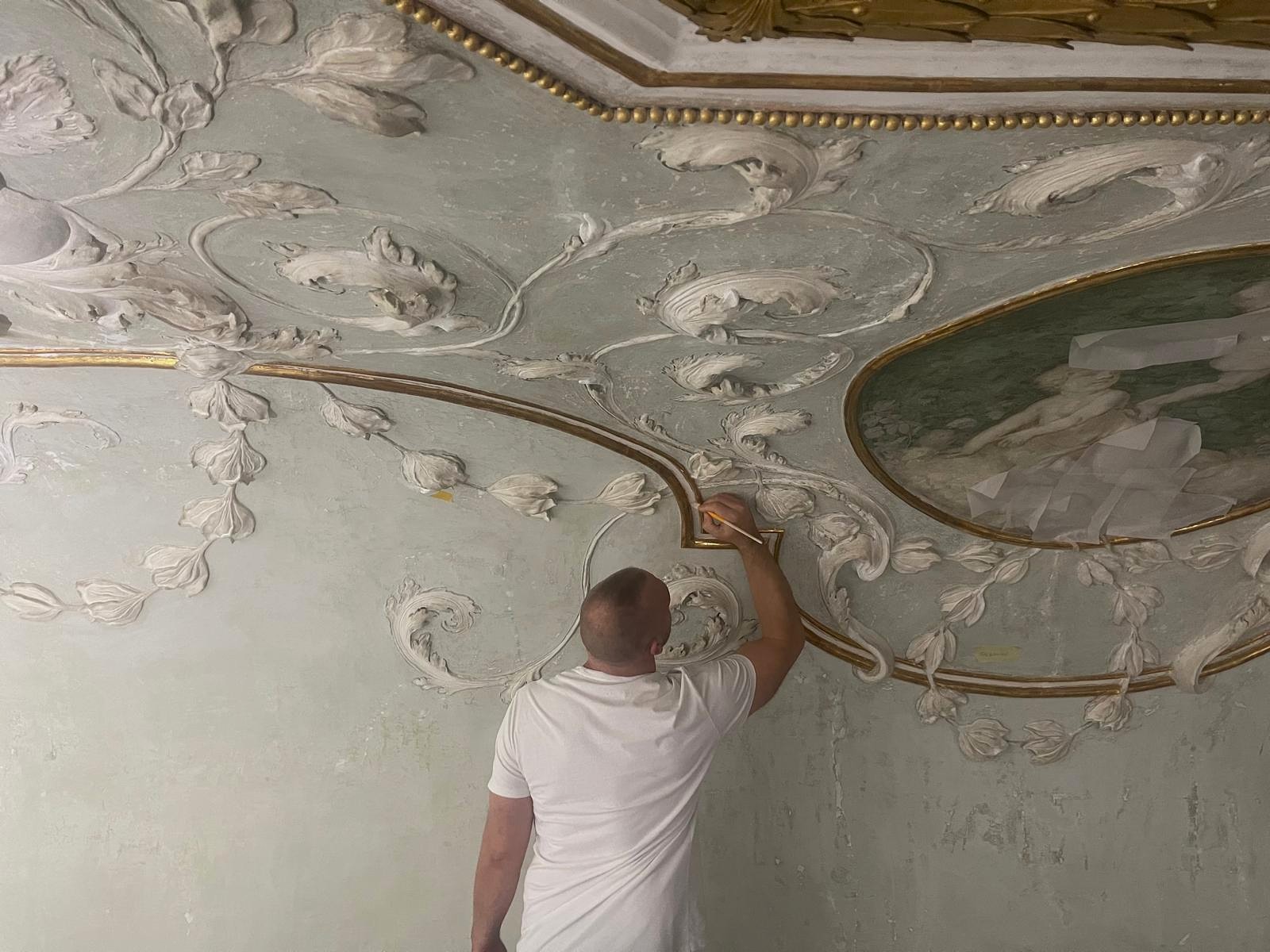 Handwerker bei der Detailarbeit an historischen Stuckornamenten mit Goldakzenten